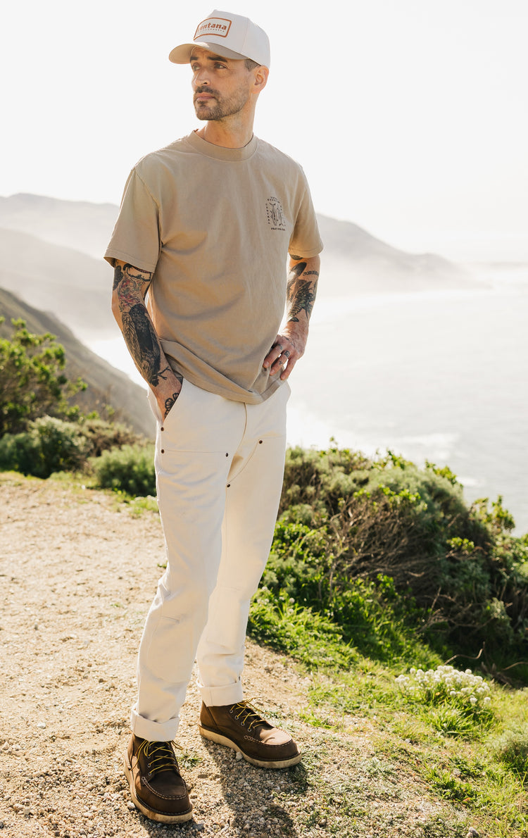 Men’s Draftsman Pant in soft washed cream cotton, featuring double-front construction and copper rivets, styled with a khaki heavyweight "Pray for Fish" graphic tee.
