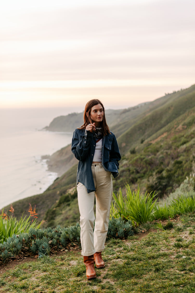Women's high-waisted Lily Pant in softwashed cream cotton, styled with an oversized men's navy corduroy shirt and brown boots for a coastal workwear look.