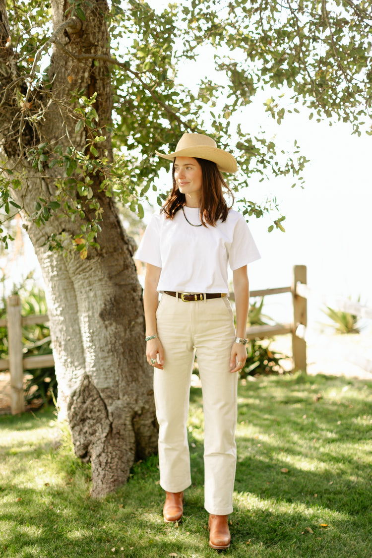 Women's high-waisted Lily Pant in softwashed cream cotton, featuring a straight-leg silhouette and durable workwear construction styled with a brown leather belt.