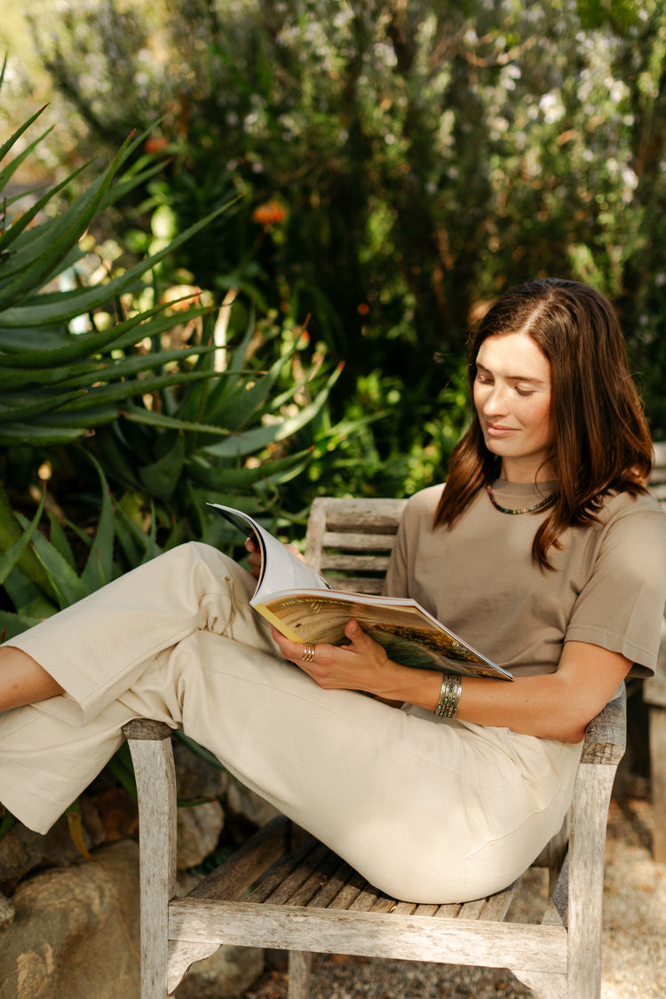 Lifestyle view of the women's Lily Pant in softwashed cream, showcasing the relaxed straight-leg fit and durable 100% cotton canvas in a garden setting.