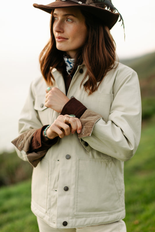 Women's cream canvas chore jacket featuring adjustable corduroy-lined cuffs, antique bronze buttons, and triple needle stitching for durability.