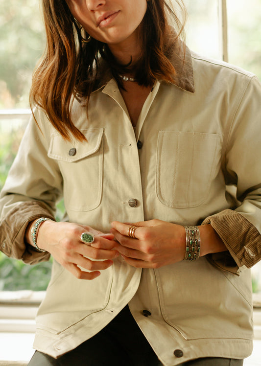 Women's cream canvas chore coat showing multiple utility pockets and brown corduroy collar, styled with turquoise jewelry.