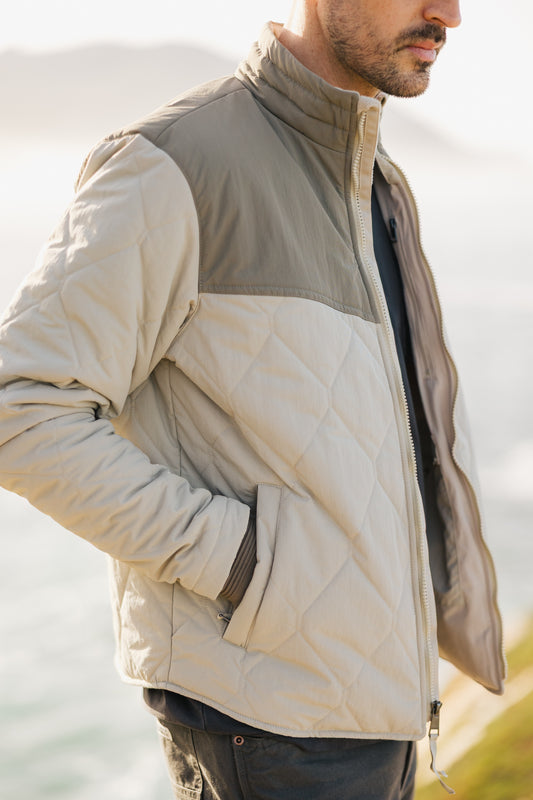 Side view of the men's Cruzer jacket in sage and cream, highlighting the zippered hand-warmer pockets and the durable diamond-quilted exterior.