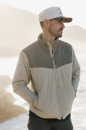 Profile view of the men's Cruzer jacket in sage and cream, paired with a two-tone camo 5-panel hat featuring a cream corduroy crown and camouflage brim.