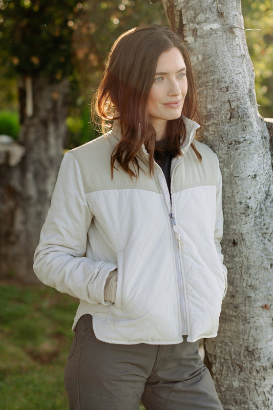 Women's Cruiser Jacket in a cream two-tone quilted design, featuring a tan shoulder yoke and zip-up front, paired with Lily Pants in salt washed vintage coal.