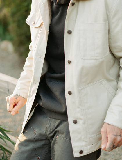 Close-up of the Draftsman Pant in Vintage Coal featuring copper-riveted double-front panels, styled with the Arroyo Rancher Jacket in cream for a rugged winter workwear look.