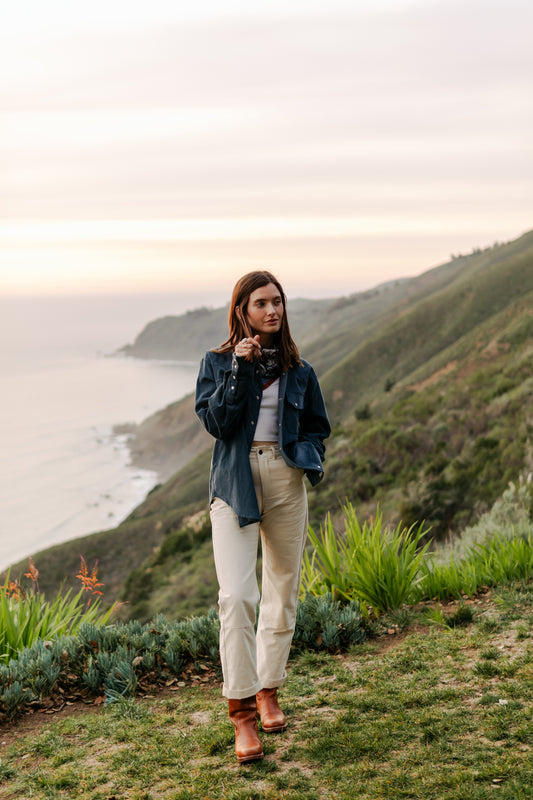 Women's high-waisted Lily Pant in softwashed cream cotton, styled with an oversized men's navy corduroy shirt and brown boots for a coastal workwear look.