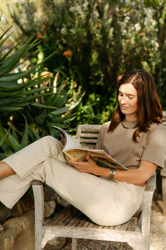 Lifestyle view of the women's Lily Pant in softwashed cream, showcasing the relaxed straight-leg fit and durable 100% cotton canvas in a garden setting.