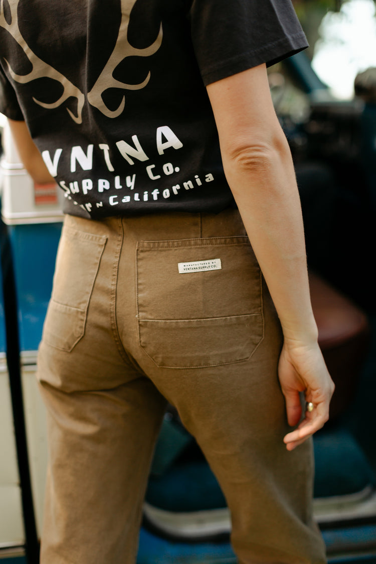 Alt Text: Close-up back view of the Tobacco Lily Pant featuring large rear patch pockets and a VNTNA Supply Co. brand label, paired with a Big Sur, California antler graphic tee.