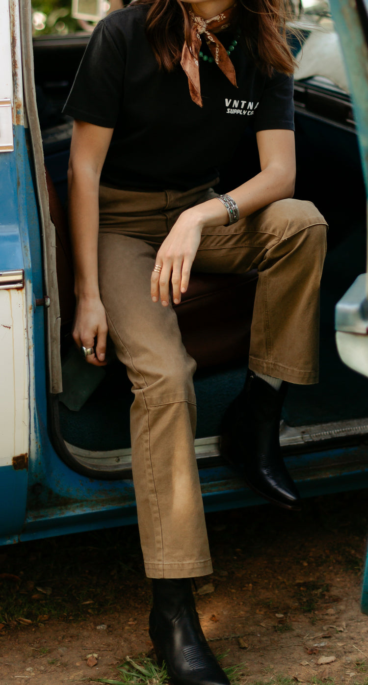 Seated view of the women's Lily Pant in Tobacco brown, highlighting the double-knee reinforcement panels and durable 100% cotton canvas construction.
