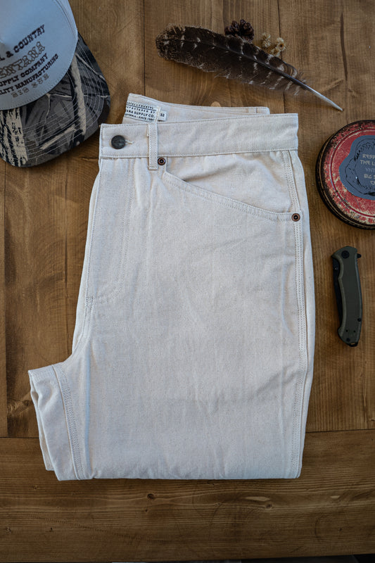 Flat-lay of the Tradesman Pant in Ivory, featuring heavy-duty triple-needle reinforced seams, copper rivets, and a custom VNTNA branded button on 100% cotton canvas.
