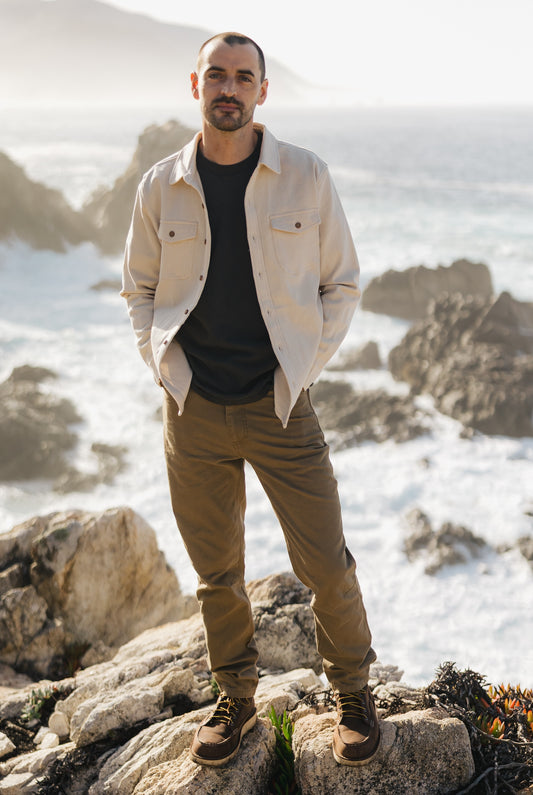 Men’s Tradesman Pant in salt washed Tobacco featuring a straight-leg silhouette and 100% cotton canvas durability, styled with a cream South Coast shirt on a coastal clif