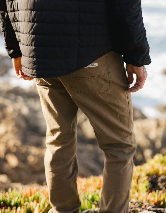 Rear view of the Tradesman Pant in salt washed Tobacco, featuring a reinforced back pocket with the VNTNA Supply Co. woven label, styled with the quilted black Stillwater Jacket.