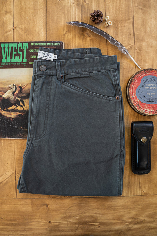 Flat-lay of the Tradesman Pant in Vintage Coal, showcasing the salt-washed charcoal texture, triple-needle stitching, copper rivets, and the VNTNA Supply Co. manufactured label on 100% cotton canvas.
