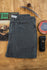 Flat-lay of the Tradesman Pant in Vintage Coal, showcasing the salt-washed charcoal texture, triple-needle stitching, copper rivets, and the VNTNA Supply Co. manufactured label on 100% cotton canvas.